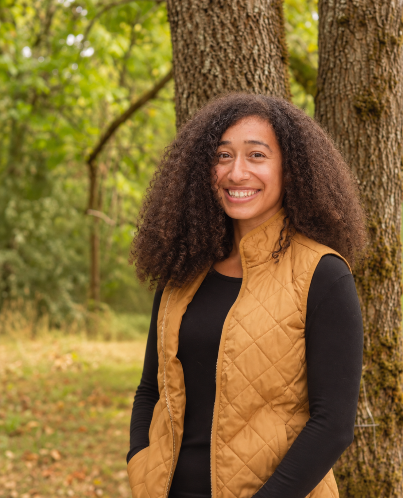 Women wearing a gold vest in front of a tree.